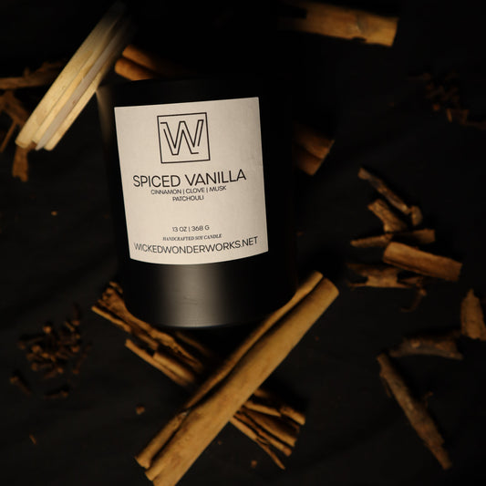 Cinnamon, clove, musk, and patchouli scented soy candle. Spiced Vanilla' by Wicked Wonder Works, styled on a black background with scattered cinnamon sticks. 