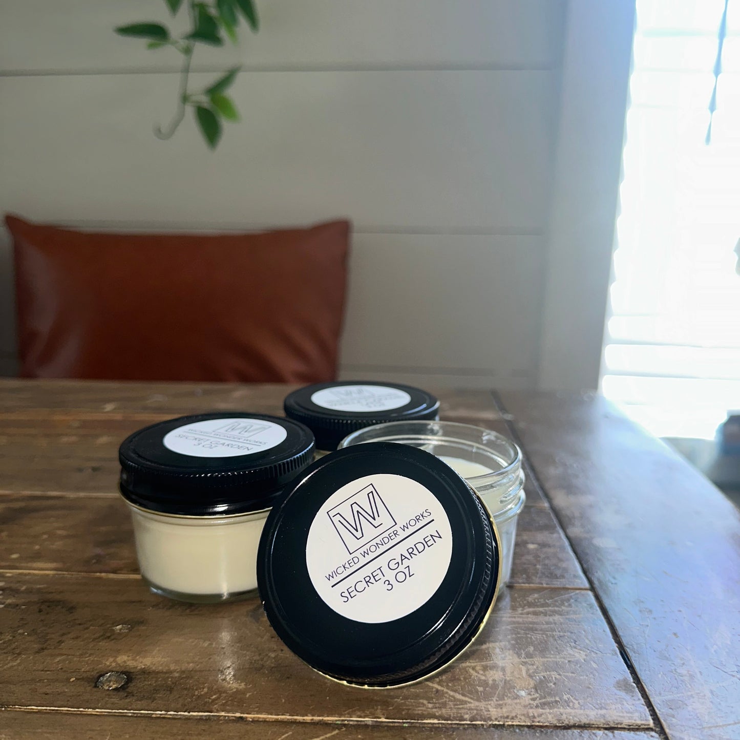 Three small jars with black lids on a wooden surface, with a blurred background.