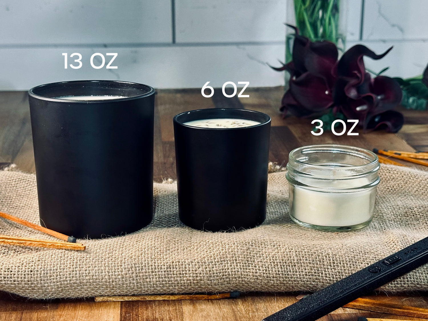 Three black candle containers with labeled sizes on a textured surface.